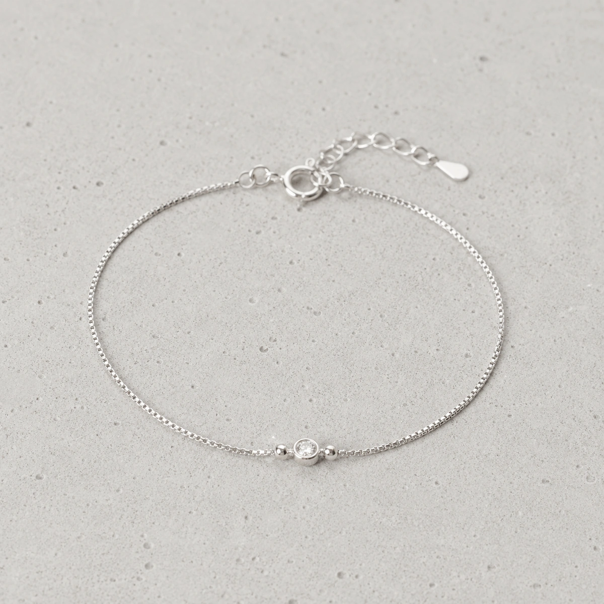 close-up van fijne minimalistische armband met subtiel steendetail op lichte betonnen achtergrond