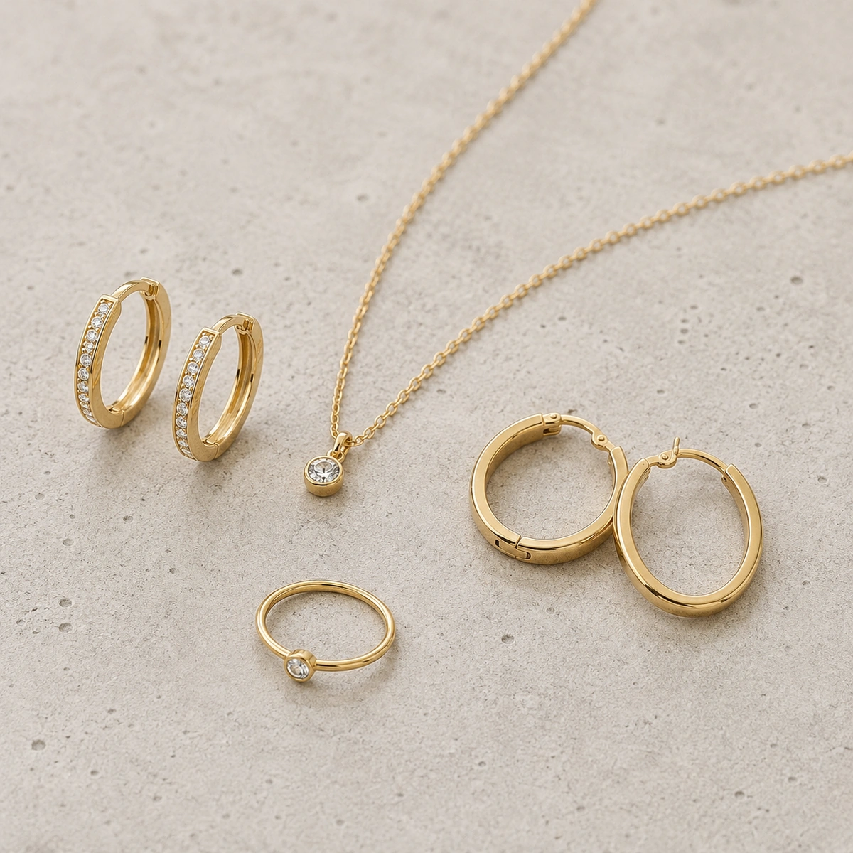 combinatie van oorringen met fijne ketting en smalle ring op lichte betonnen achtergrond